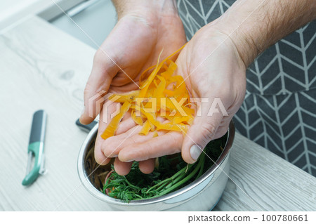 Cropped photo of man wearing apron holding carrot peelings in hands over metal bowl. Recycling, composting, fertilizing. Cropped photo of man wearing apron holding carrot peelings in hands over metal bowl. Recycling, composting, fertilizing. 100780661