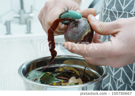 Male hands peeling fresh beetroot with peeler over bowl of vegetable peelings closeup. Separate waste collection. 100780667
