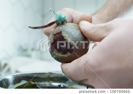 Close-up of unrecognizable man wearing peeling beet with peeler knife over bowl full of peelings, standing in kitchen. Close-up of unrecognizable man wearing peeling beet with peeler knife over bowl full of peelings, standing in kitchen. 100780668