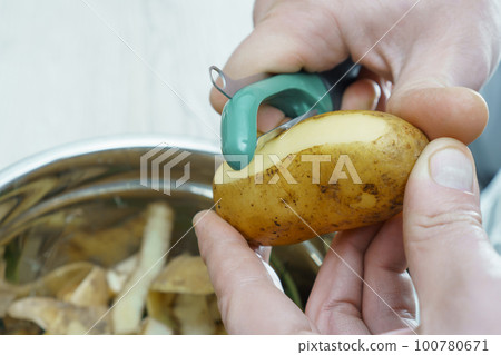 Close-up of unrecognizable man wearing peeling potato with peeler knife over metal bowl full of peelings. Composting. Close-up of unrecognizable man wearing peeling potato with peeler knife over metal bowl full of peelings. Composting. 100780671