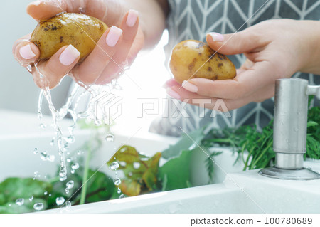 Female manicured hands washing fresh potato under water jet in kitchen sink closeup. Cooking, prepare ingredients. 100780689