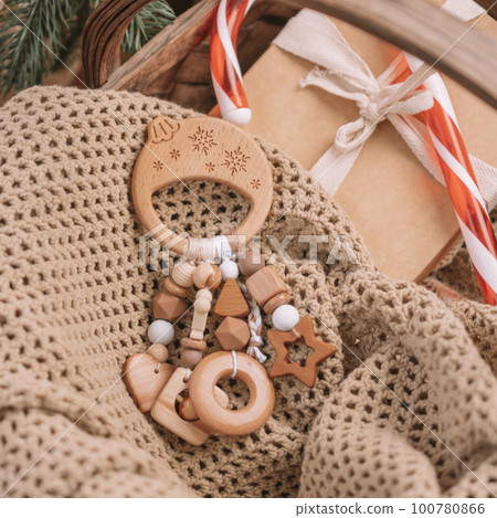 Wooden Christmas ball-shaped childrens teether with silicone beads lies among gifts on blanket under Christmas tree 100780866