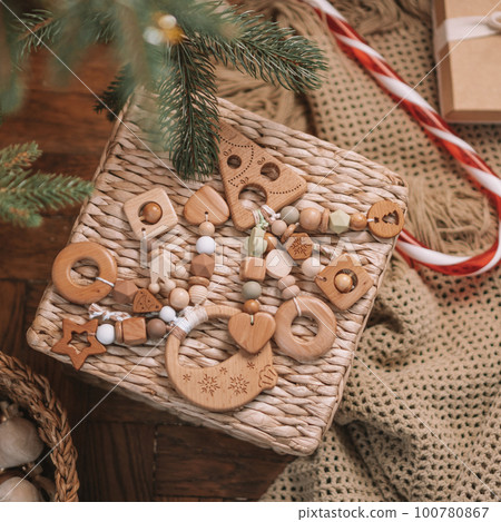 Wooden Christmas tree and ball shaped childrens teethers with silicone beads lie on wicker basket under Christmas tree 100780867