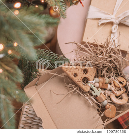 Wooden Christmas tree-shaped children's teether with silicone beads lies among gifts in open box under Christmas tree 100780868