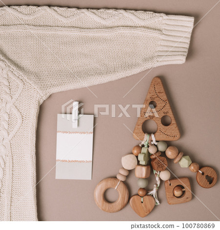 Wooden Christmas tree shaped childrens teether with silicone beads with sweater and card on beige background. Copy space 100780869