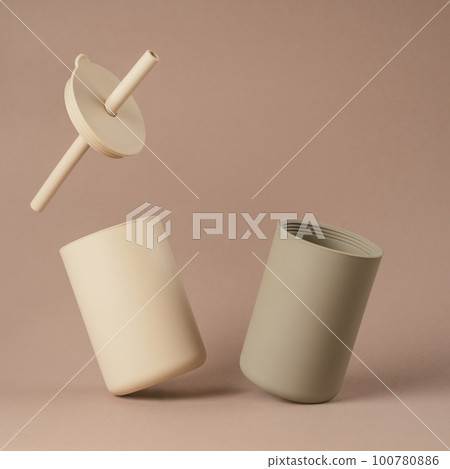 Modern colorful pastel beige and grey silicone sippy glasses with straws standing by side on brown background. 100780886