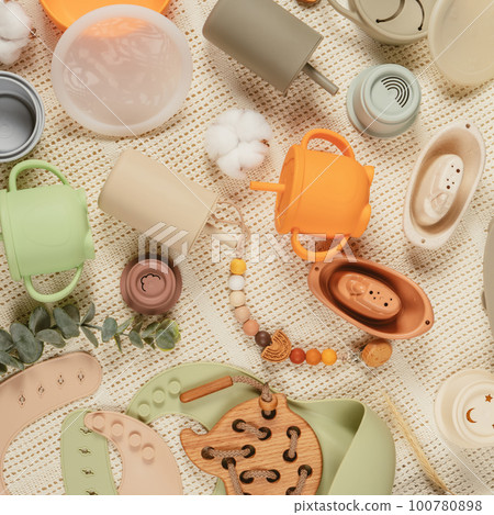 Pastel silicone collection of tableware, cutlery, bibs, accessories and wooden toys for children on cloth background. 100780898