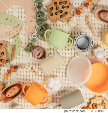 Pastel silicone kit of tableware, cutlery, bibs, accessories and wooden toys for children on white cloth background. Pastel silicone kit of tableware, cutlery, bibs, accessories and wooden toys for children on white cloth background. 100780900