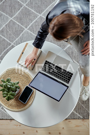 Young woman using laptop and making notes in notebook sitting at workplace at home, remote work top view Young woman using laptop and making notes in notebook sitting at workplace at home, remote work top view 100781192