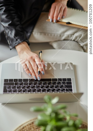 Close up woman hand using laptop and making notes in notebook sitting at workplace at home, remote work Close up woman hand using laptop and making notes in notebook sitting at workplace at home, remote work 100781209
