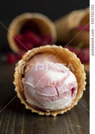 Waffle cone with white pink cream ice cream and raspberries Waffle cone with white pink cream ice cream and raspberries 100782102