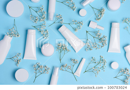 White plastic tubes, jars, and gypsophila branches on a blue background, containers for cosmetic creams and gels, advertising and brand promotion White plastic tubes, jars, and gypsophila branches on a blue background, containers for cosmetic creams and gels, advertising and brand promotion 100783024