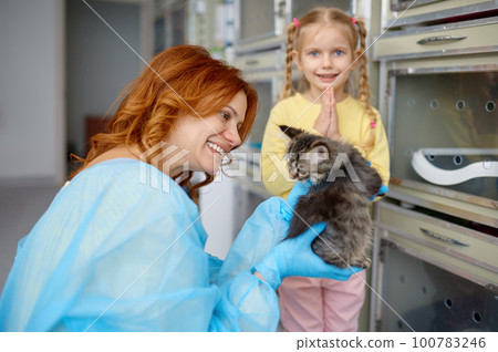 Mother holding little kitten and her daughter folding hand in pray position 100783246
