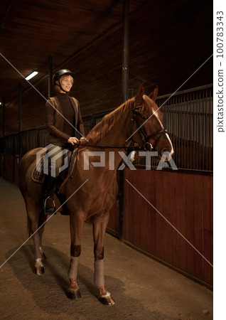 Smiling woman rancher riding out stable on horse 100783343
