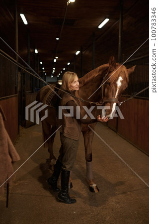 Horsewoman petting horse stroking animal muzzle over stable interior Horsewoman petting horse stroking animal muzzle over stable interior 100783346