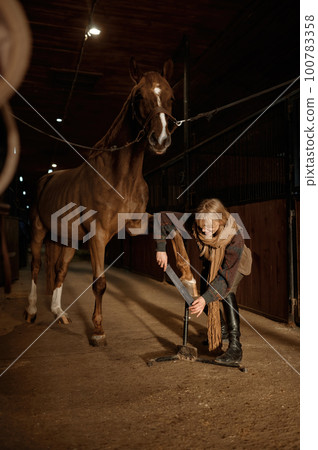 Young woman making horses hoof manicure, filing and shaping horseshoe 100783358