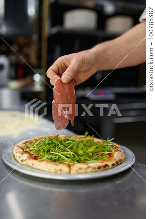 Closeup chef hand holding slice of bacon over pizza Closeup chef hand holding slice of bacon over pizza 100783387