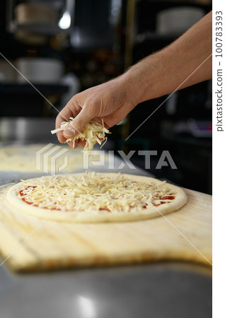 Pizza preparation process with closeup chef hands sprinkling cheese 100783393