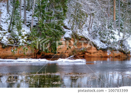 Red sandstones on the bank of the river Salaca. Red sandstone rock in Bezdeligu winter. Skanaiskalns nature park 100783399