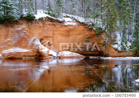 Red sandstones on the bank of the river Salaca. Red sandstone rock in Bezdeligu winter. Skanaiskalns nature park 100783400