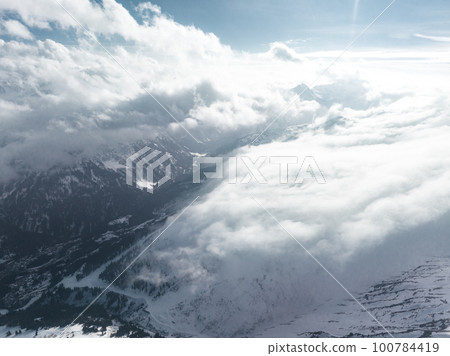 Alpine landscape with peaks covered by snow and clouds. Magical clouds covering peaks of the mountains at the famous St. Anton am Arlberg ski resort. 100784419