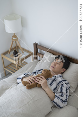 A man in his 50s sleeping with a teddy bear, morning 100787783