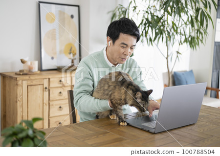 一個 50 多歲的男人在一個有貓的房間裡做文案工作 100788504
