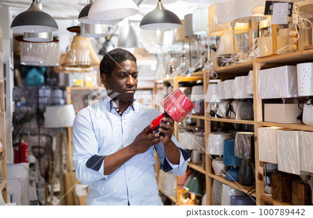 Man chooses table lamp in an electrical store Man chooses table lamp in an electrical store 100789442