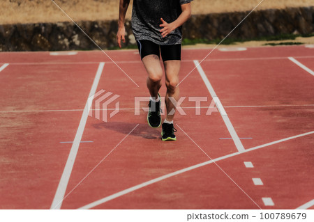 Male runner making a start dash on the track of the athletics stadium 100789679