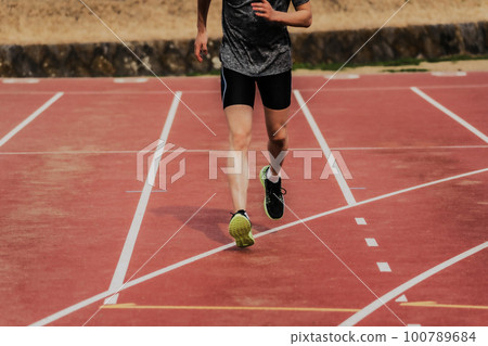 Male runner running on athletic track 100789684