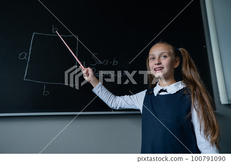 The schoolgirl answers at the lesson. Caucasian girl writes a formula on a blackboard. 100791090