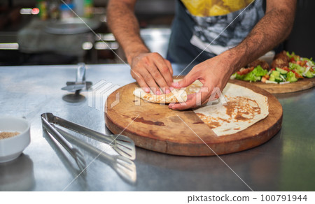 A chef prepares a falafel plate and tortillas on a round wooden cutting board in the kitchen. A chef prepares a falafel plate and tortillas on a round wooden cutting board in the kitchen. 100791944