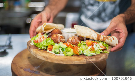 Presenting the middle eastern Lebanese dish Falafel on a wooden plate. tortilla, vegetable salad, and tahini sauce. Presenting the middle eastern Lebanese dish Falafel on a wooden plate. tortilla, vegetable salad, and tahini sauce. 100791946