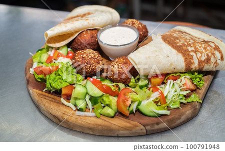 Delicious Falafel dish on a wooden plate close-up. tortilla, vegetable salad, and tahini sauce. Delicious Falafel dish on a wooden plate close-up. tortilla, vegetable salad, and tahini sauce. 100791948