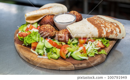 Delicious starter Falafel dish on a wooden plate in the Lebanese restaurant kitchen. flatbread, vegetable salad, and tahini sauce. Delicious starter Falafel dish on a wooden plate in the Lebanese restaurant kitchen. flatbread, vegetable salad, and tahini sauce. 100791949