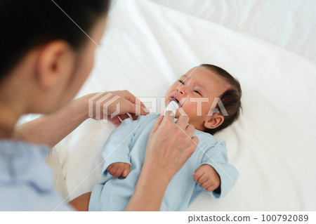 mother using finger to clean newborn baby mouth (tongue and gum) with clean gauze on bed 100792089