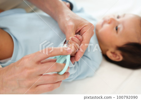 mother cutting baby's hand fingernails with nail scissors. 100792090