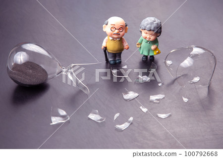miniature people. a couple of elderly people near a broken hourglass. 100792668