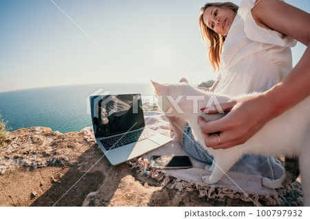 Woman sea laptop. Business woman petting cat and working on laptop by the sea. Close up on hands of pretty lady typing on computer outdoors summer day. Freelance, digital nomad and holidays concept. 100797932