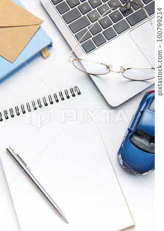 Modern white office desk table with laptop, notebook, toy car and other supplies. 100799214