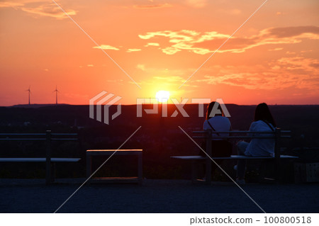 Rear view of two girls sitting on a bench at sundown in Bottrop, Germany in the Ruhr area 100800518