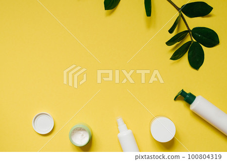 Set of organic SPA cosmetics with green leaves. Top view of bottles made of white recyclable plastic on a yellow background with a copy space. Packaging design of natural cosmetic products for skin 100804319