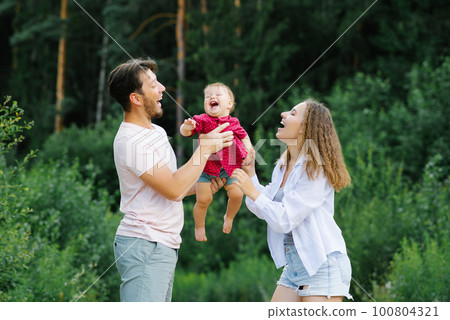 Happy young parents with a baby are walking through the forest, having fun and enjoying happy moments 100804321