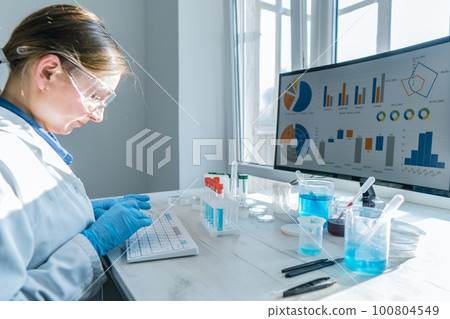 A female researcher sits at a workplace in a laboratory, behind a personal computer monitor.  100804549