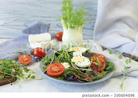 Salad of microgreens, lettuce, tomatoes, cheese and boiled eggs, on a plate 100804896