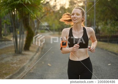 Athletic woman in sportswear running at morning in public park with beautiful sunlight. Fitness, sport and healthy lifestyle concept 100806486