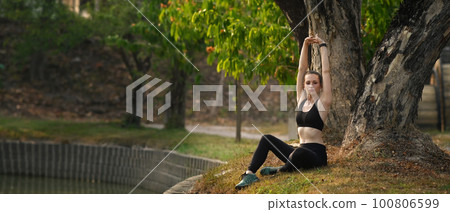 Happy athletic woman sitting in green park, warming up her arms before doing exercise. Fitness, training and healthy lifestyle concept Happy athletic woman sitting in green park, warming up her arms before doing exercise. Fitness, training and healthy lifestyle concept 100806599