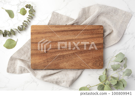 Wood cutting board on linen napkin with leaves on marble 100809941