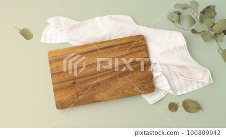 Wooden cutting board on napkin with leaves on green background Wooden cutting board on napkin with leaves on green background 100809942
