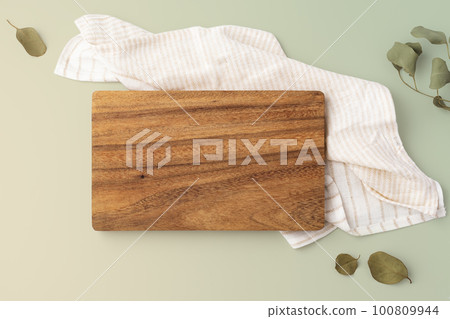 Cutting board on napkins with leaves on green background, top view Cutting board on napkins with leaves on green background, top view 100809944